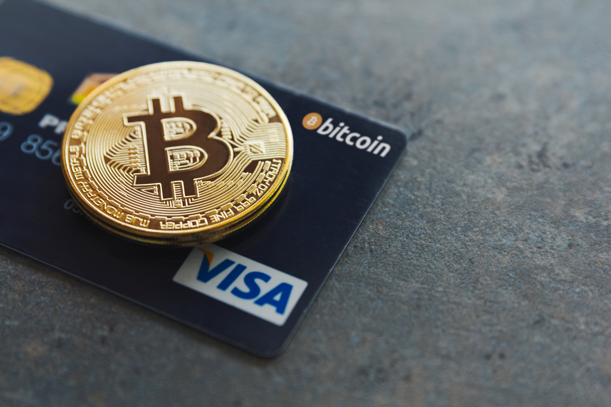 ALT Text:  An image of a Visa card with a Bitcoin coin placed on top, symbolizing the integration of Bitcoin as a form of currency for Visa transactions.